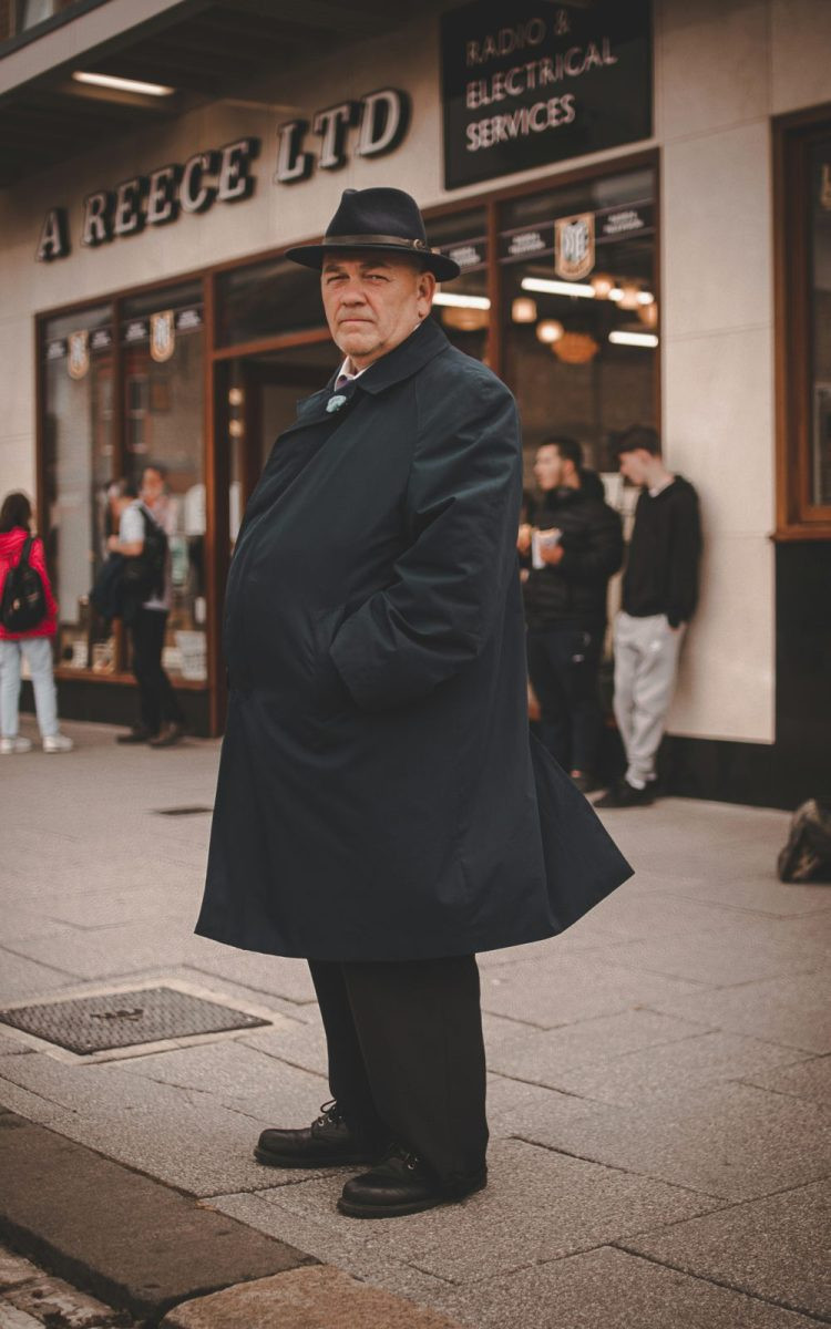 Man in a dark long coat and hat outdoors