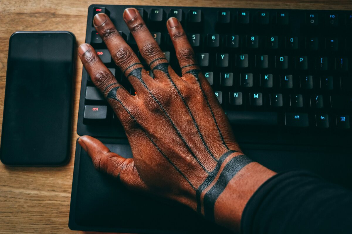 Man's hand on a keyboard with thin line band tattoos across his fingers