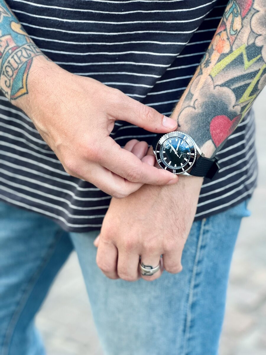 Tattooed man in a striped shirt wearing a ring on his ring finger