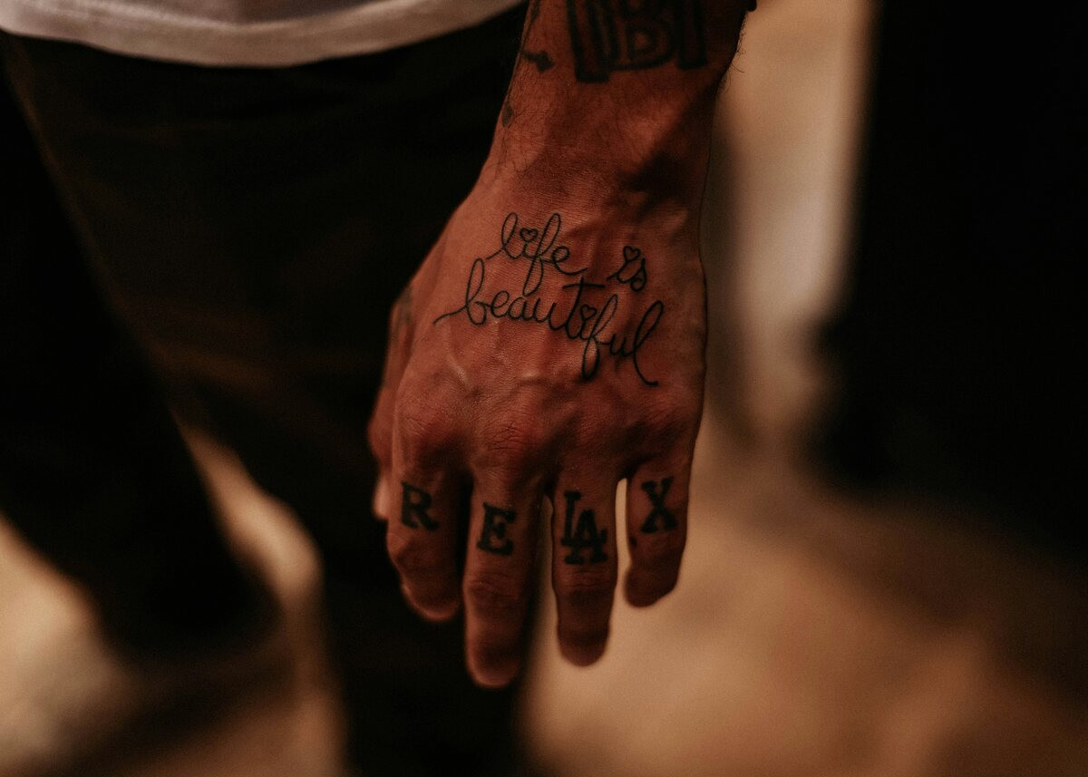 Man's hand with script lettering and RELAX tattooed across his fingers