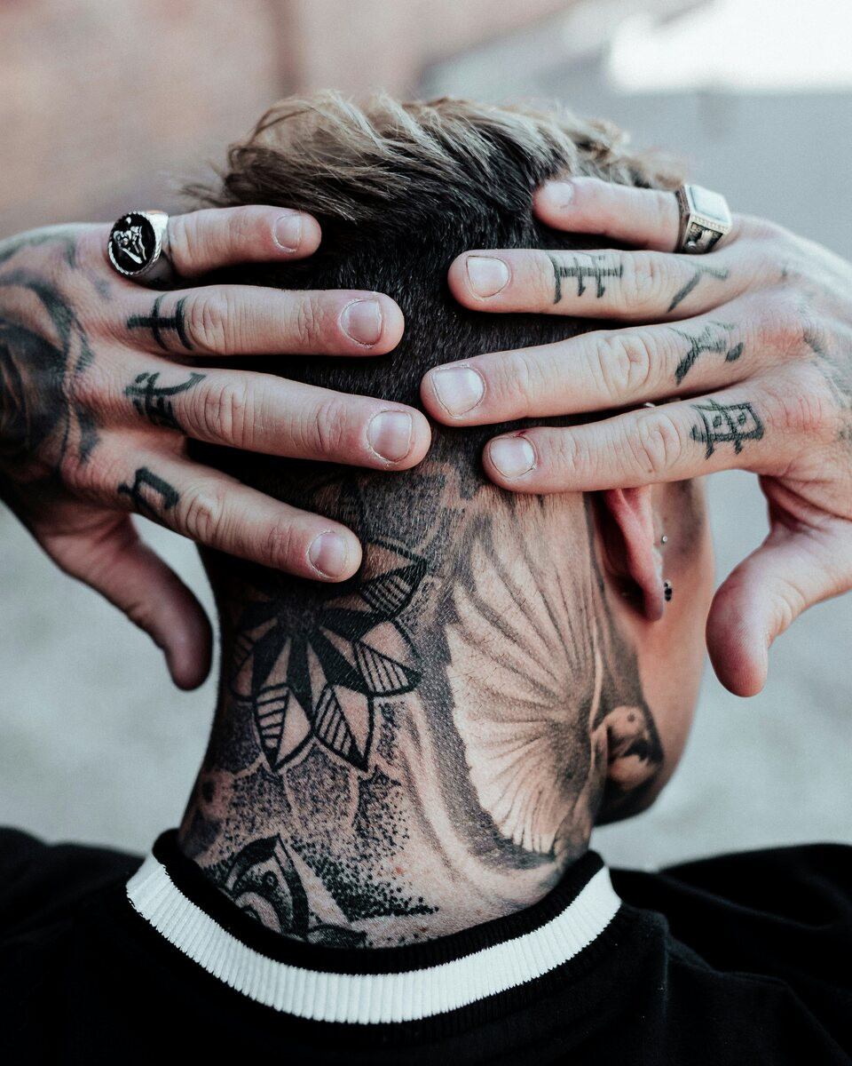 Man with small symbol tattoos on his fingers, hands behind his head