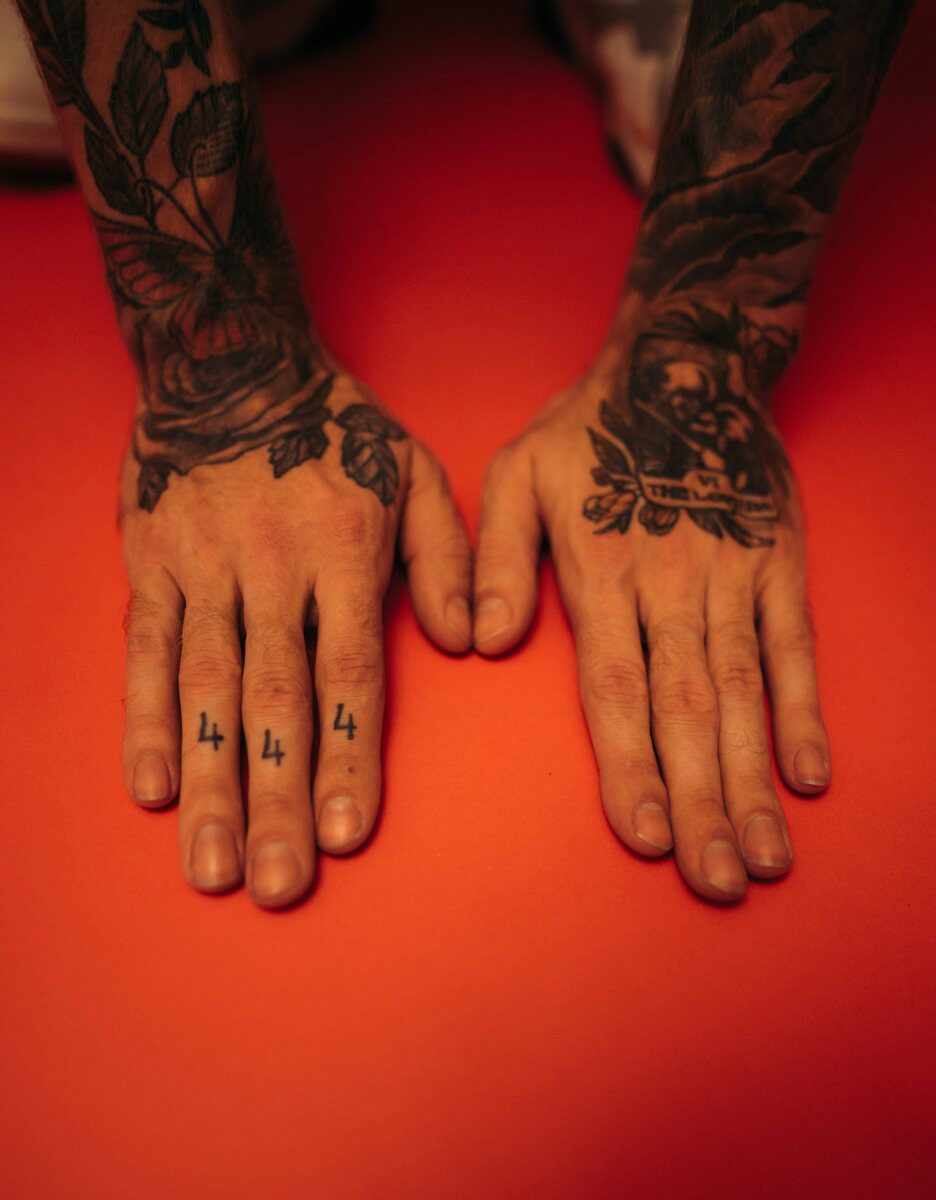 Tattooed hands on a red background with 444 tattooed on the fingers