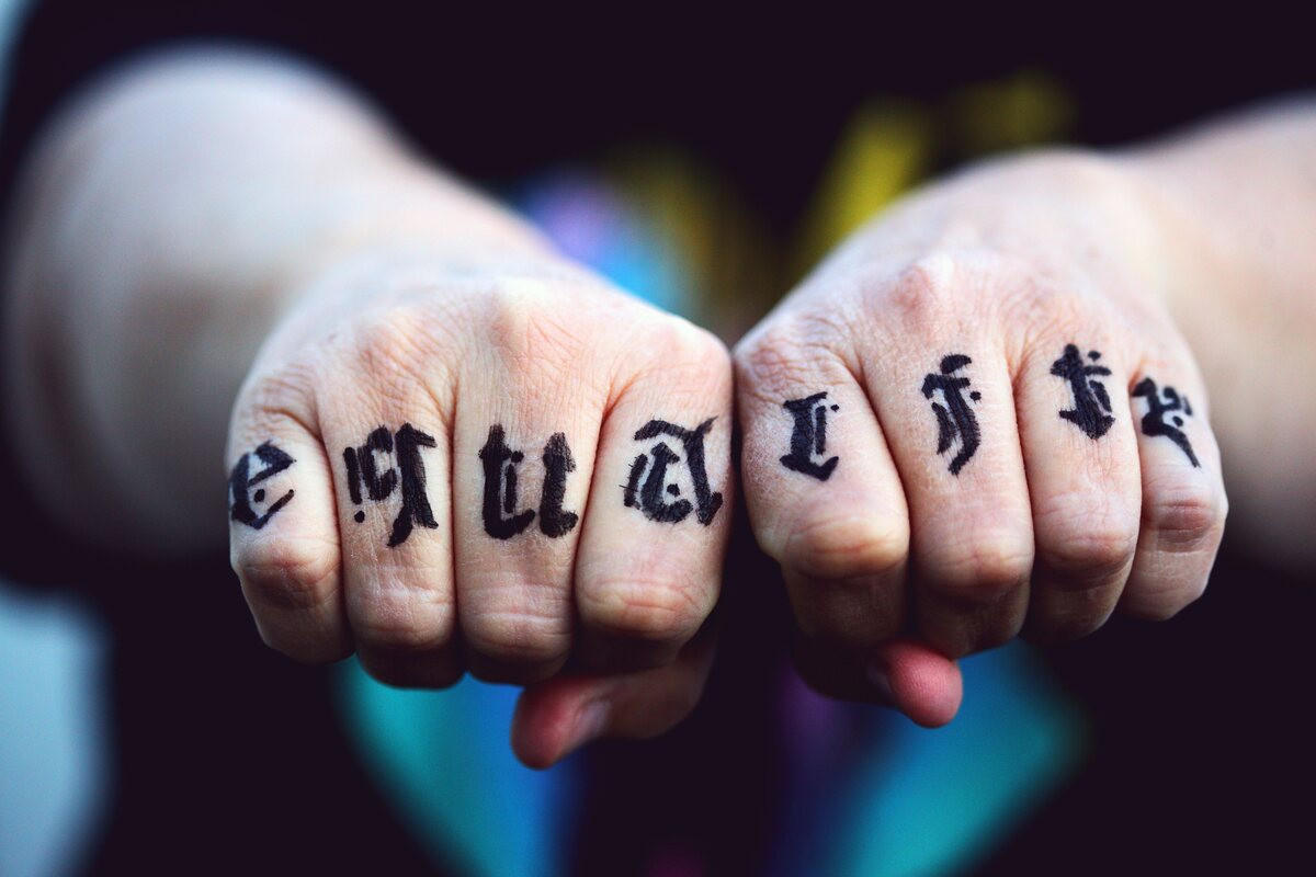 Two fists with bold blackletter tattoos across the knuckles