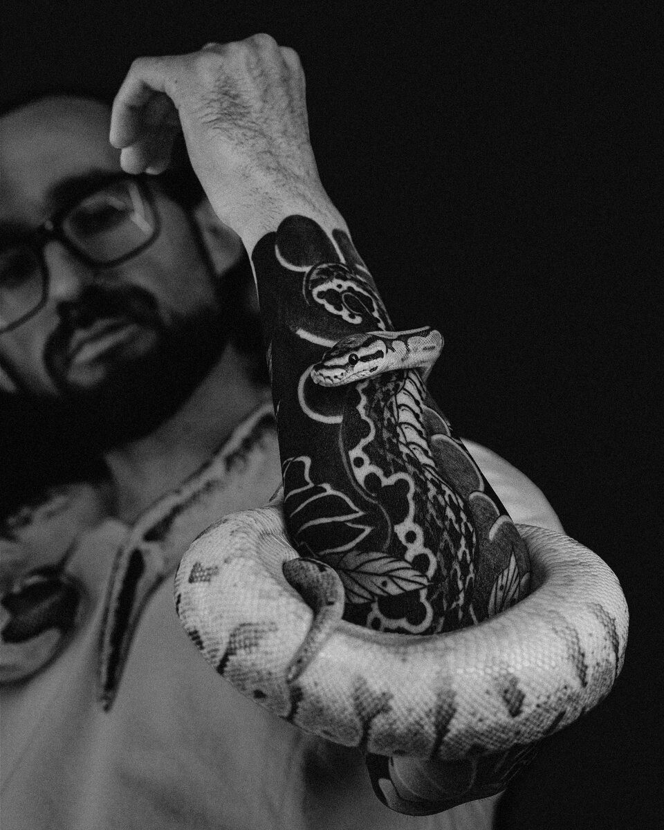 Bearded man with a blackwork arm and hand holding a snake
