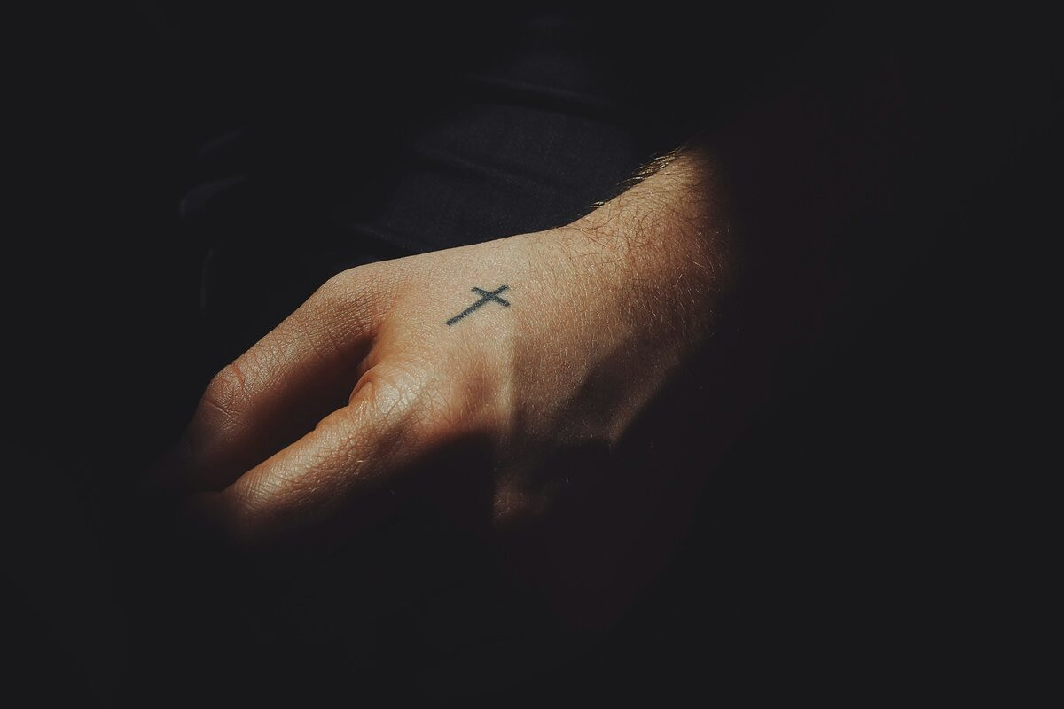 Man's hand with a small cross tattoo in low light