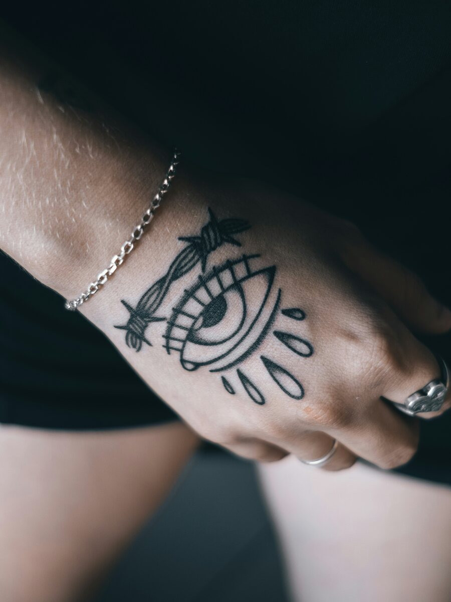 Hand with a bold black eye tattoo, chain bracelet and ring