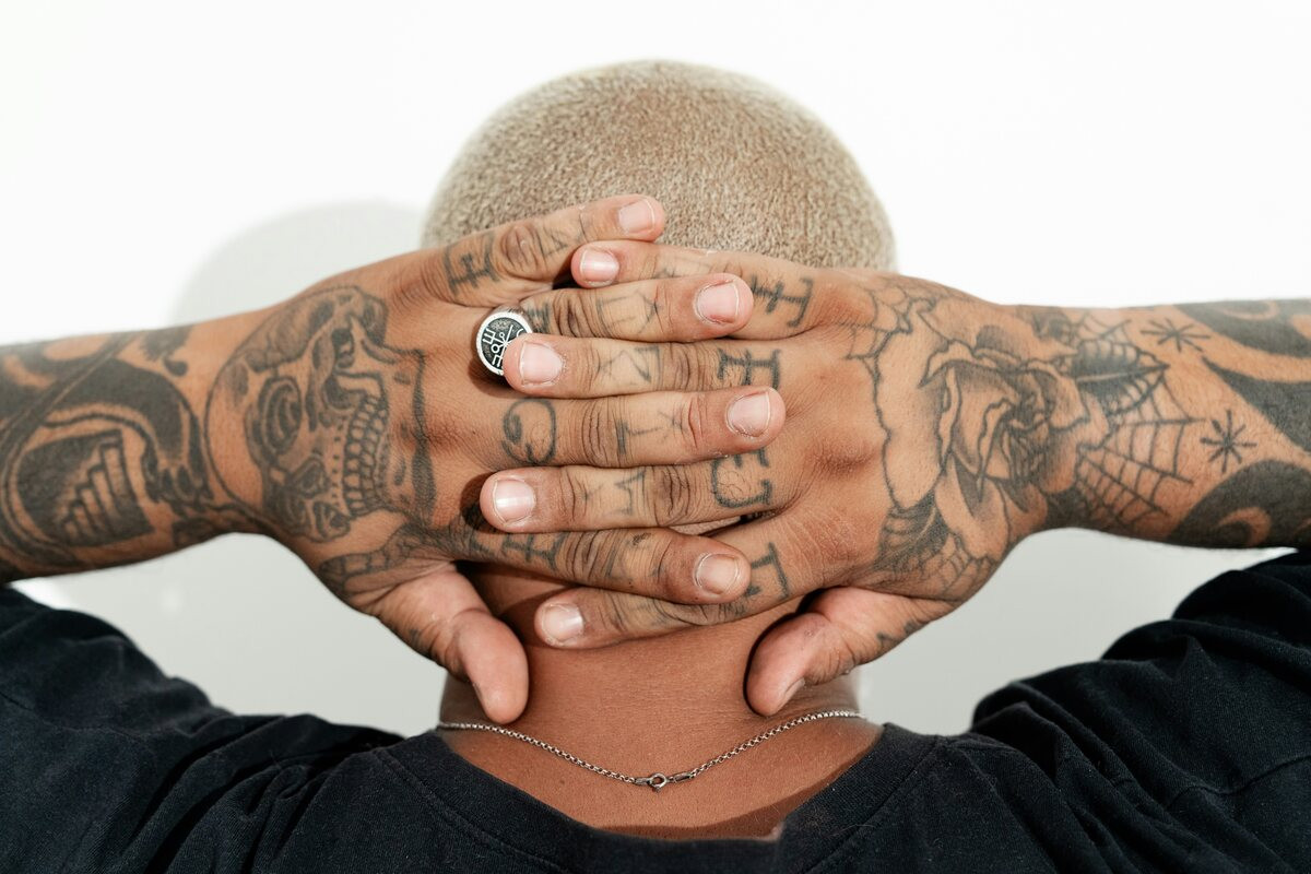 Man with hands behind his head showing finger glyphs, a skull, roses and a spiderweb