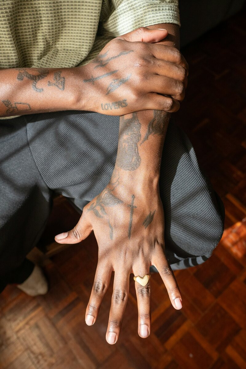 Man's heavily tattooed hands and fingers crossed over his knee